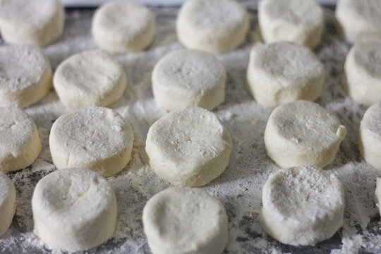 Uncooked homemade syrnyky arranged on a floured wooden board