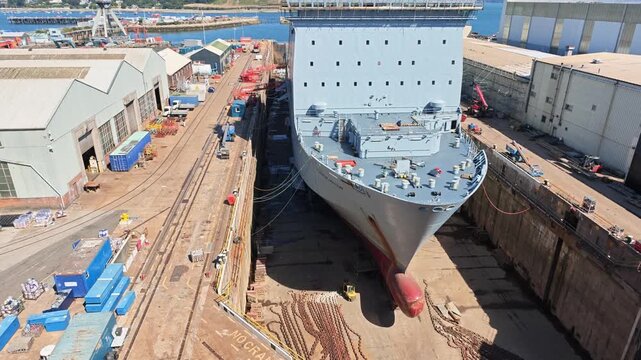 Falmouth Cornwall England UK.  18.08.2026. Video.A grey British warship sits in a dry dock for repairs with industrial cranes and shipyard buildings visible in the background on a sunny day
