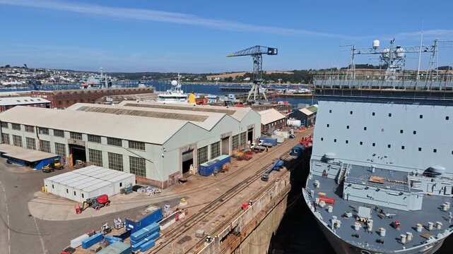 Falmouth Cornwall England UK.  18.08.2026. Video.A grey British warship sits in a dry dock for repairs with industrial cranes and shipyard buildings visible in the background on a sunny day
