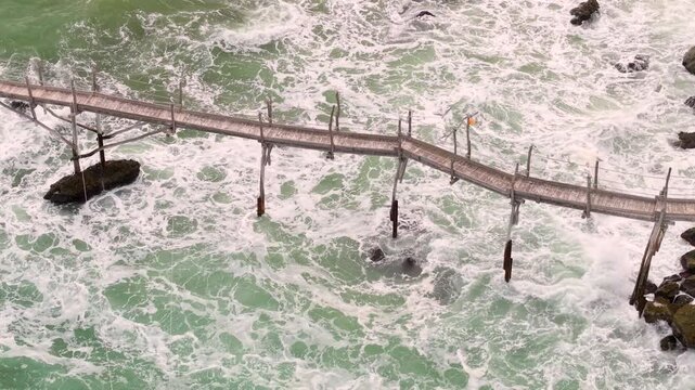  Aerial top down drone tracking along long wooden pier revealing Trabocco Turchino in San Vito Chietino Abruzzo Italy. Unique Italian cultural heritage stilt house over crashing waves 4K