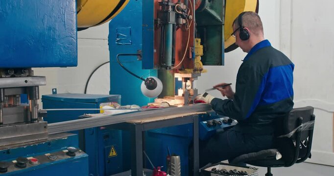 Metal component production with press operator bending blanks on stamping press. Blue collar employment in industrial metalworking, medium shot