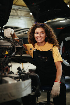 Woman mechanic smiling while repairing car engine in workshop