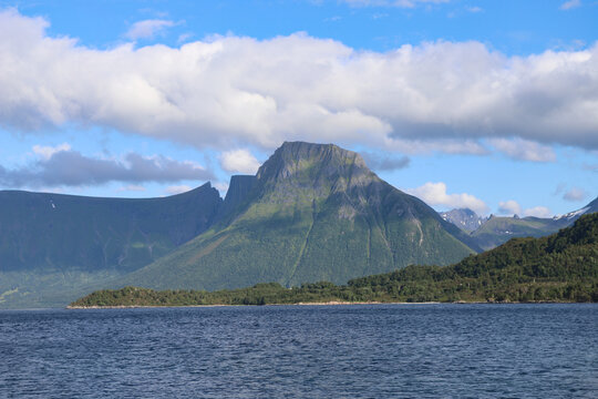 Scenic view of a majestic green mountain rising above a fjord on Hareid island, Norway. Picturesque norwegian fjord scenery with a prominent mountain under a partly cloudy sky.