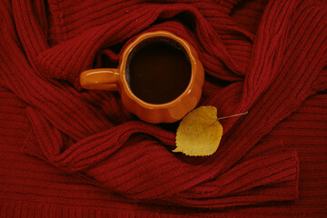 Obraz premium An orange mug of coffee resting on a red knitted sweater beside an open book and a yellow autumn leaf, with soft film grain, high quality photo