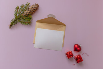 Flat lay of kraft envelope with blank card, fir branch, red heart, and gifts on smooth pink background. © tatiana
