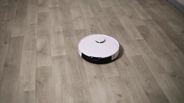 White robotic vacuum cleaner autonomously moving on a modern wooden laminate floor, providing convenient and smart automated house cleaning for a comfortable and effortless lifestyle at home
