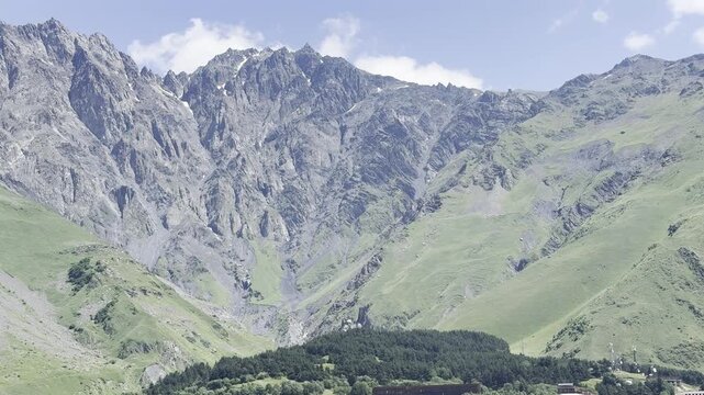 Majestic rocky mountain peaks and green alpine slopes with a forest at the base under a blue sky in a scenic natural landscape