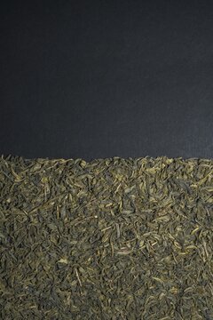Dried green tea leaves along the bottom of a dark textured background, leaving generous copy space above.