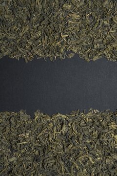 Dried green tea leaves arranged along the top and bottom edges of a dark background with central copy space.