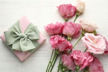 Fototapeta premium Beautiful eustoma flowers and gift box on white wooden table, flat lay