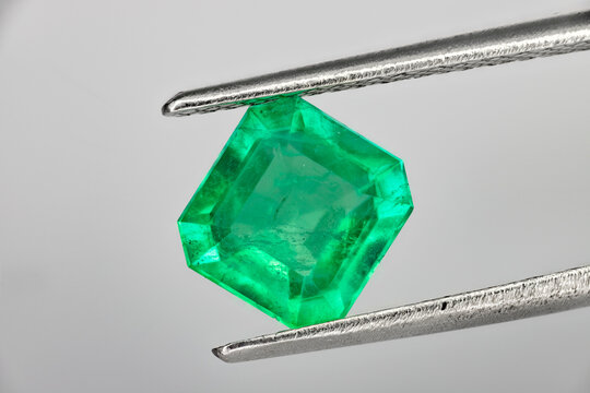 Colombian emerald cut green gemstone held in tweezers, close-up macro on white background 3