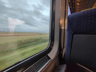 Obraz premium View from a train window of fields and countryside under a cloudy sky