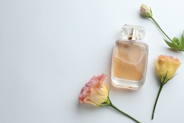 Fototapeta premium Bottle of perfume and flowers on white background, flat lay. Space for text