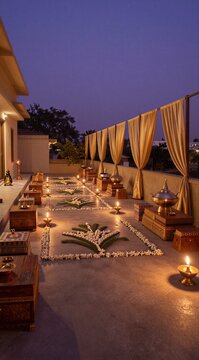 Stunning rooftop terrace decorated with traditional Indian flower rangoli, glowing brass oil lamps, wooden chests, and flowing sheer curtains under a serene twilight sky