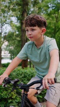 Focused boy cycles through green park along riverbank path