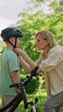 Mother fits helmet on boy before bicycle ride in green park