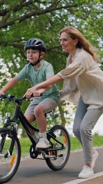 Mother supports son cycling along quiet riverside park path