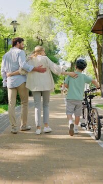 Family walks with son holding bike along sunny park path together