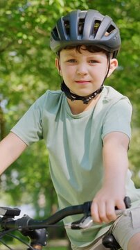 Boy smiles while sits on bicycle seat resting in green park