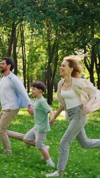 Mother cheerful father and energetic young son run through park