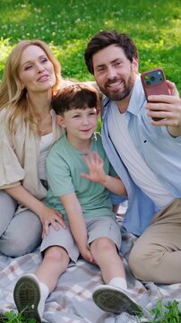 Mother father and son sit on soft picnic blanket in city park