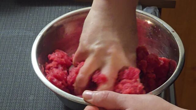 Close up of hands kneading fresh raw minced beef meat in metal bowl preparing delicious homemade burgers meatballs or meatloaf recipe in home kitchen. Video 4k