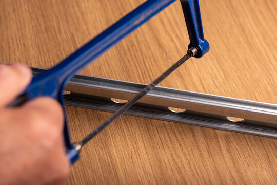 A hand with a metal saw is cutting a rail for wallmount.