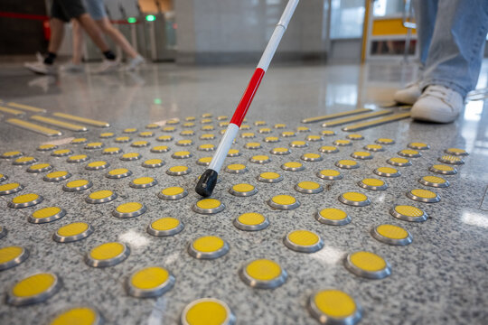 A blind woman walks on tactile paving. Close-up of her feet and a walking stick.
