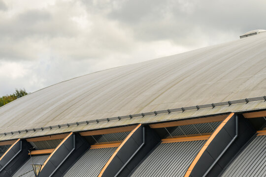 Curved metal building roof beneath dramatic cloudy sky.