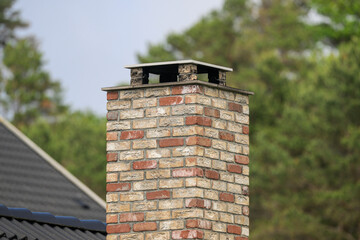 Close view of weathered brick chimney against trees. © Trygve