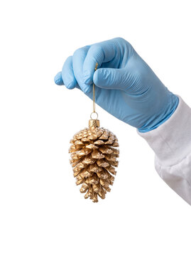 A Hand in a Blue Medical Glove Holding a Gold Christmas Tree Ornament Shaped Like a Pine Cone Isolated