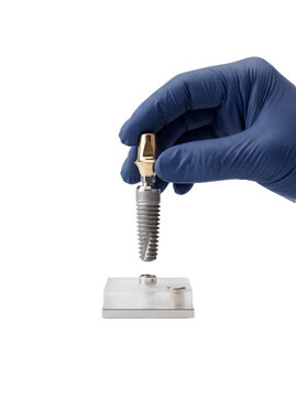 Dental surgeon hand in blue glove holding a titanium dental implant post over a laboratory display model, transparent background