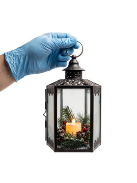Person wearing medical latex gloves holding a vintage Christmas lantern with pine needles and glowing candle, transparent background