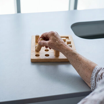 Close-up of an elderly person exercising fine motor skills with a wooden pegboard during occupational therapy