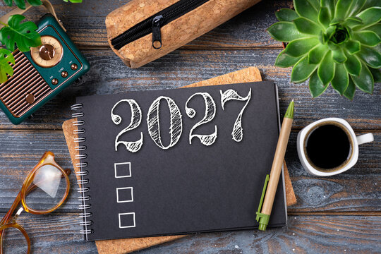 New year resolutions 2027 on desk. 2027 goals list with notebook, coffee cup, plant on wooden table. Resolutions, plan, goals, action, checklist, idea concept. New Year 2027 resolutions, copy space