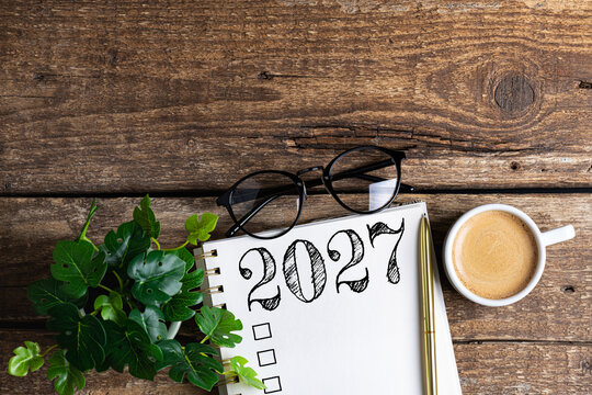 New year resolutions 2027 on desk. 2027 goals list with notebook, coffee cup, plant on wooden table. Resolutions, plan, goals, action, checklist, idea concept. New Year 2027 resolutions, copy space