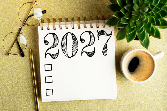 2027 New year resolutions on desk. 2027 goals list with notebook, coffee cup, plant on golden background. Resolutions, plan, goals, action, checklist, idea concept. New Year 2027 resolutions