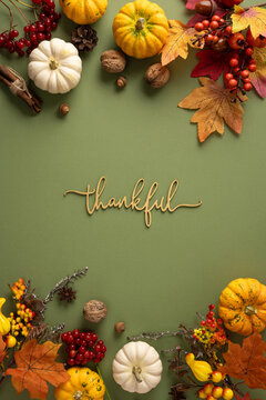 Thankful autumn flat lay with pumpkins, leaves and Thanksgiving decorations on vertical pastel background with text Thankful