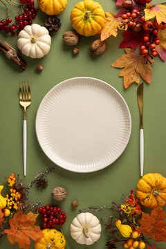 Autumn Thanksgiving table setting with pumpkins, fall leaves, nuts and empty plate for dinner on green pastel color copy space