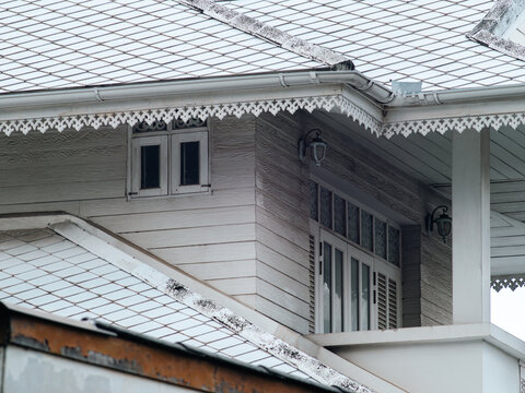 Traditional Thai colonial style house corner with diamond patterned roof, ornate white trim, shuttered windows and gutters, heritage architecture detail