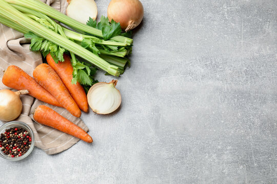 Fresh celery stalks, carrots, onion bulbs and spices on grey table, flat lay. Space for text