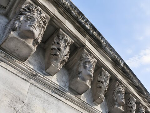 Row of carved stone corbel heads with stylised faces along a civic cornice