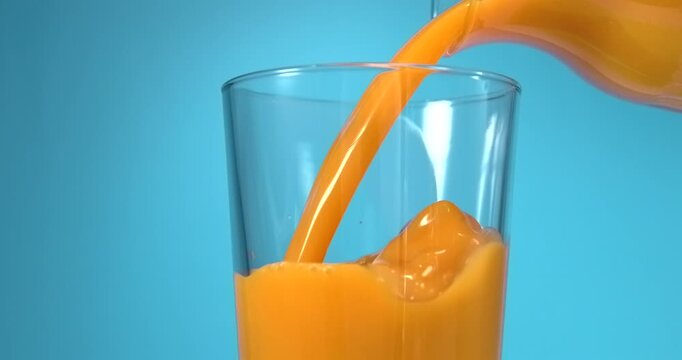 Fruit juice pouring from bottle into glass in slow motion on blue background
