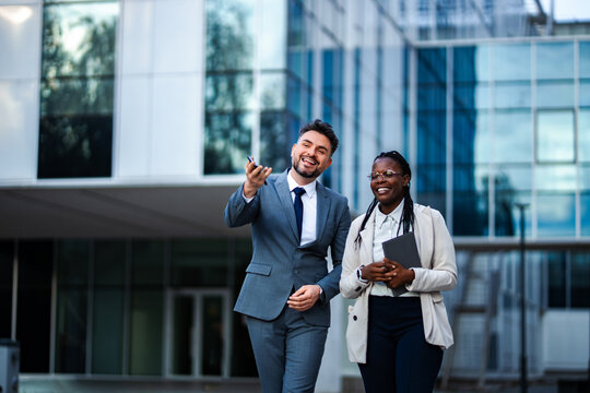 Business colleagues walking and laughing outdoors in front of office building