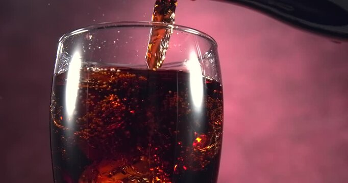 Cola pouring into glass with ice cubes in slow motion on red background