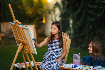 Young sisters painting together outdoors developing creativity © Jelena