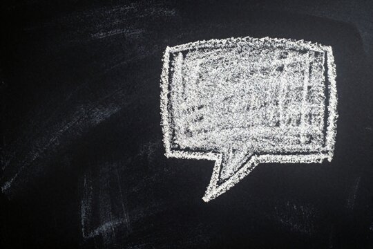 White chalk speech bubble on black blackboard background. Hand drawn empty text box for message dialogue. Blank communication symbol with rough texture provides copy space for text. Conceptual icon