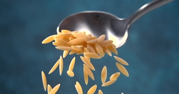 Orzo pasta falling from a spoon in slow motion on blue background