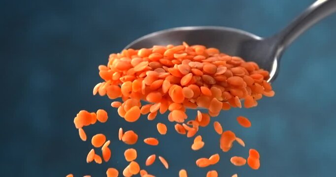 Red lentils falling from a spoon in slow motion on blue background