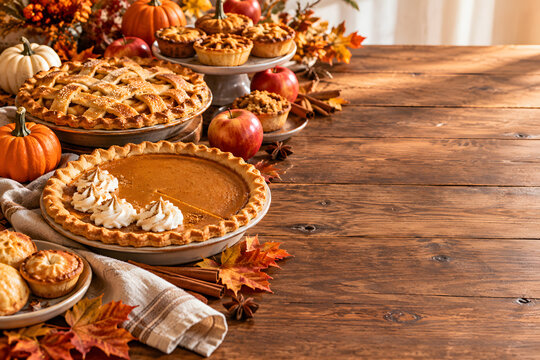 Thanksgiving dessert table with pumpkin pie, apple pie, mini pastries, apples and pumpkins on a rustic wooden table, warm autumn light and generous copy space.